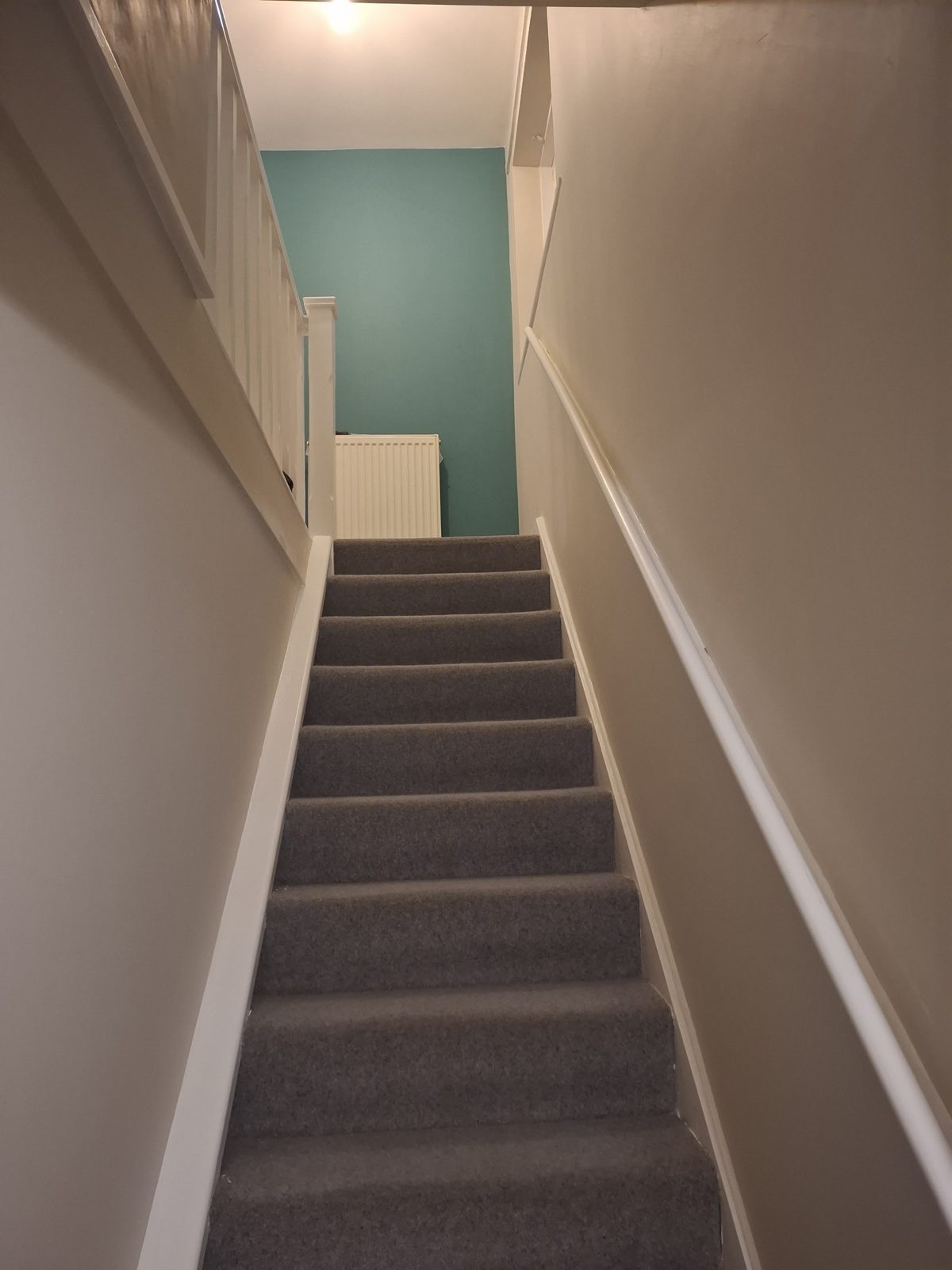 Freshly decorated staircase with crisp white woodwork leading up to a teal landing