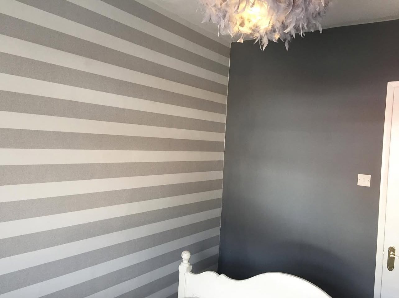 Bedroom with a grey and white striped wall beside a smooth charcoal painted wall