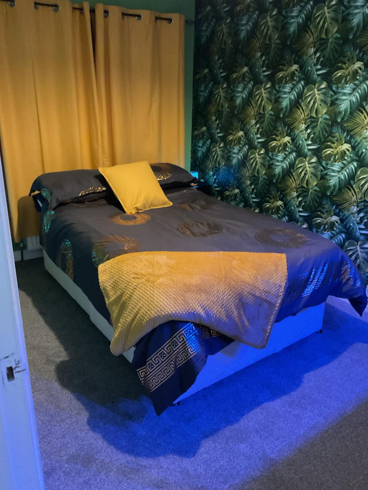 Bedroom with a dark green jungle leaf feature wall and mustard curtains
