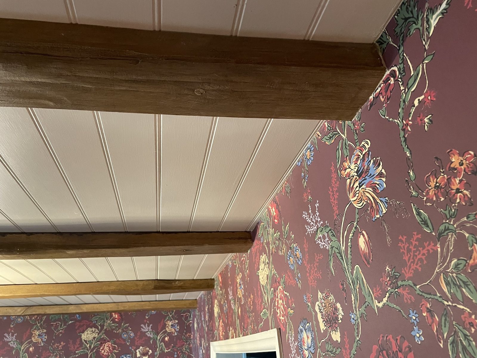 Burgundy floral wallpaper beneath a white panelled ceiling with dark timber beams